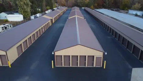 Storage buildings with paved access and tree-lined backdrop at Lambertville Mini Storage Secor.