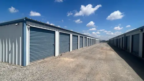 Drive-up storage units with roll-up doors and wide gravel access lanes at Texoma Self Storage.