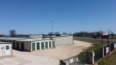 Wide driveways and rows of storage units at Trio Self Storage with fence and monument sign visible.